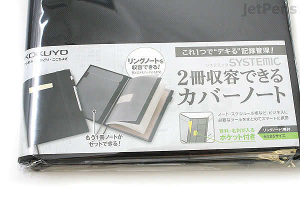 A packaged KOKUYO Systemic Cover Notebook in black fabric, A5 size, with ring binding and 6 mm ruled pages. The packaging shows an image of the notebook open with two sections inside.