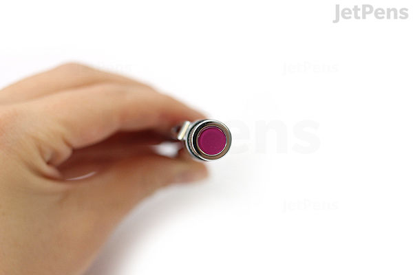 Close-up of a hand holding a Retro 51 Tornado Classic Lacquers rollerball pen with a pink body, shown from the top end, highlighting the pen's circular metallic cap with a pink center.