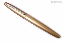 A gold-colored Pilot Metropolitan fountain pen with a smooth, plain finish and a medium nib, shown closed and angled slightly to the left on a white background.