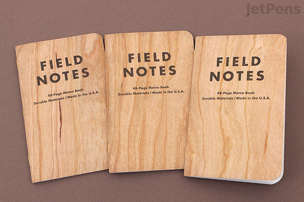 Three Field Notes memo books with cherry wood-patterned covers, each labeled "FIELD NOTES" in uppercase letters. The books measure 3.5 by 5.5 inches and contain 48 pages of graph paper. They are arranged side by side on a brown surface.