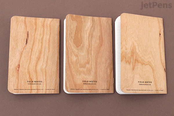 Three Field Notes memo books with cherry woodgrain covers, each measuring 3.5 by 5.5 inches, arranged side by side on a brown surface. The covers display natural wood patterns and the text "FIELD NOTES" along with product details at the bottom center.