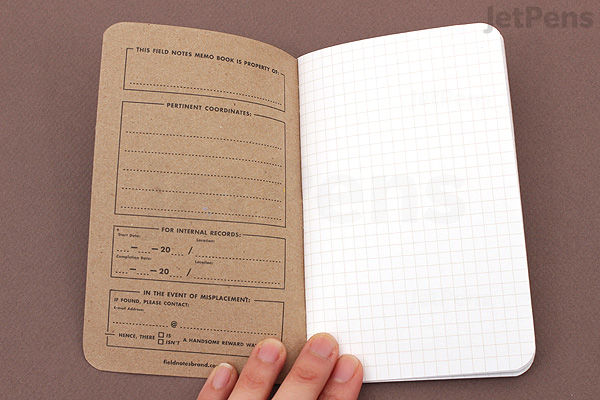 Open Field Notes Cherry Graph Memo Book showing a left page with printed form fields and a right page with a blank graph grid. The notebook measures 3.5" x 5.5" and has 48 pages. Hand holding the bottom edge.