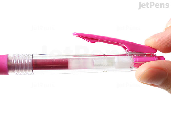 A close-up image of a hand holding a Zebra Sarasa Clip gel pen with a 0.3 mm tip in magenta color. The pen has a clear barrel showing the ink inside and a magenta clip on the cap.