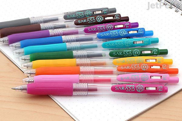 A set of Zebra Sarasa Clip gel pens with 0.4 mm tips, arranged in a row on a notebook. The pens have translucent barrels and clips, and come in various vibrant colors including black, blue, green, orange, pink, and purple.
