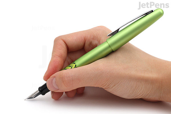A hand holding a green marble Pilot Metropolitan Retro Pop fountain pen with a fine nib, poised to write on a white surface.