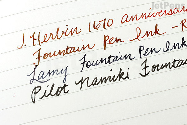 Close-up of handwritten text on lined paper showing different fountain pen inks in red, blue, and black, demonstrating smooth writing on an Apica Premium C.D. A5 notebook with 5 mm graph lines.