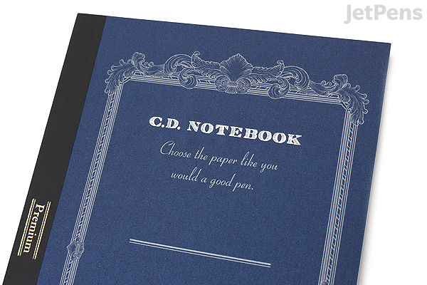 A close-up photo of an Apica Premium C.D. Notebook with a dark blue cover featuring ornate white decorative borders and text. The notebook is A5 size with 7 mm ruled lines. The cover text includes "C.D. NOTEBOOK" and a cursive phrase beneath it.