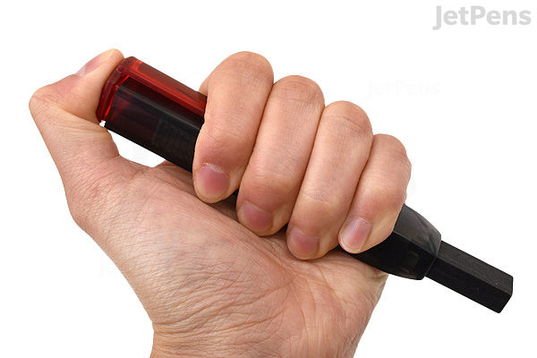 A hand holding a black Sakura Sumo Grip retractable eraser with a red translucent top.