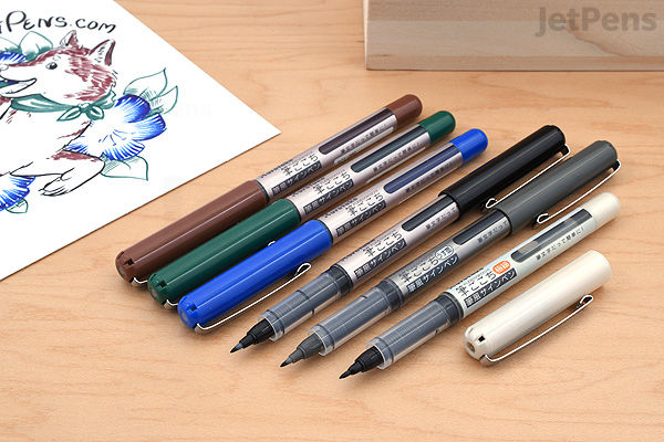 Set of four Kuretake Fudegokochi regular brush pens in different colors, displayed uncapped with tips visible, alongside a partially visible floral ink drawing on paper.