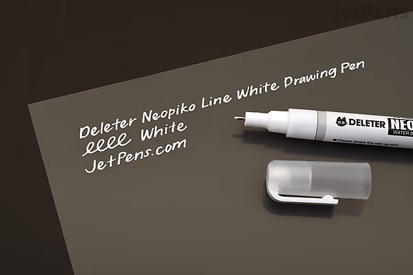 Deleter Neopiko Line White Drawing Pen with 0.5 mm tip, shown uncapped on a dark surface with white handwritten text beside it. The pen has a white barrel and a clear cap placed nearby.