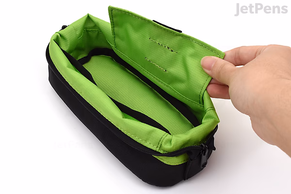 A hand holding open a black pen case shaped like a boat, revealing a bright green interior with a zippered pocket inside.