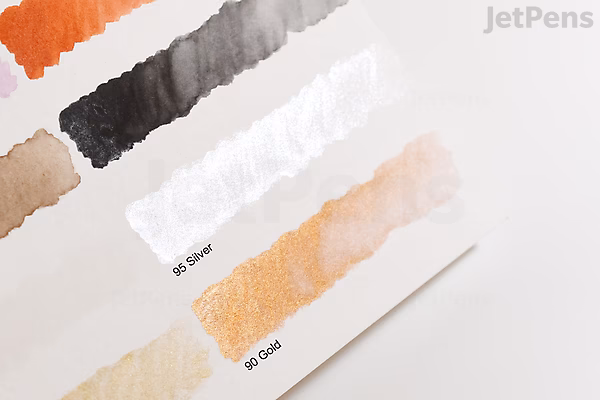 Swatches of Kuretake Gansai Tambi Watercolor paint in Silver (No. 95) displayed on white paper, showing a range of shades from light to dark in smooth brush strokes.