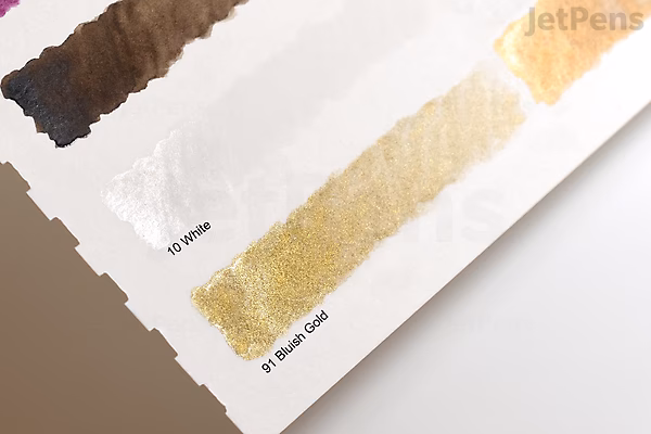 A close-up photo of a watercolor paint swatch sheet showing three metallic paint samples labeled "01 Brown," "12 Pearl Gold," and "13 Pearl Silver." The paint strokes are shiny and reflective, demonstrating the colors' shimmer on white paper.