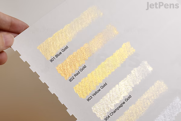 Swatches of Kuretake Gansai Tambi Watercolor Silver (No. 95) showing different shades and effects on white paper, with a hand holding the paper on the left side. The colors range from light to darker silver tones with a metallic sheen.