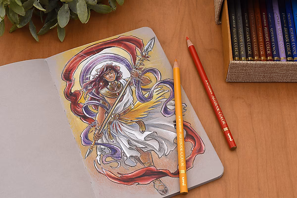Open Stillman & Birn Nova Sketchbook with a colorful drawing of a flowing, abstract figure. Two colored pencils lie on the page, and a wooden box with colored pencils is visible nearby.