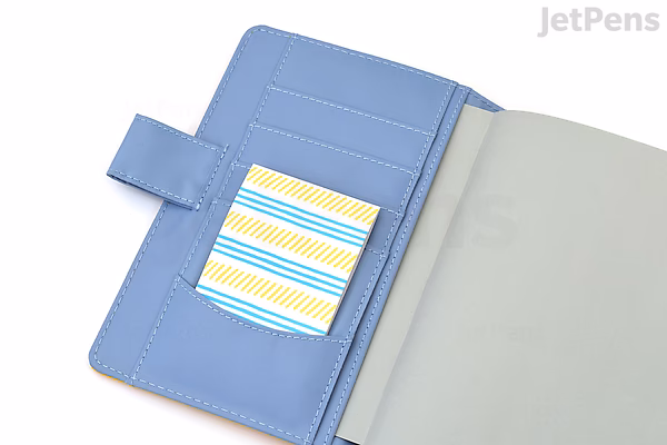 A blue planner or notebook with a snap closure, containing a small sheet of King Jim Kitta Washi Tape featuring an airmail design with blue, yellow, and white stripes.
