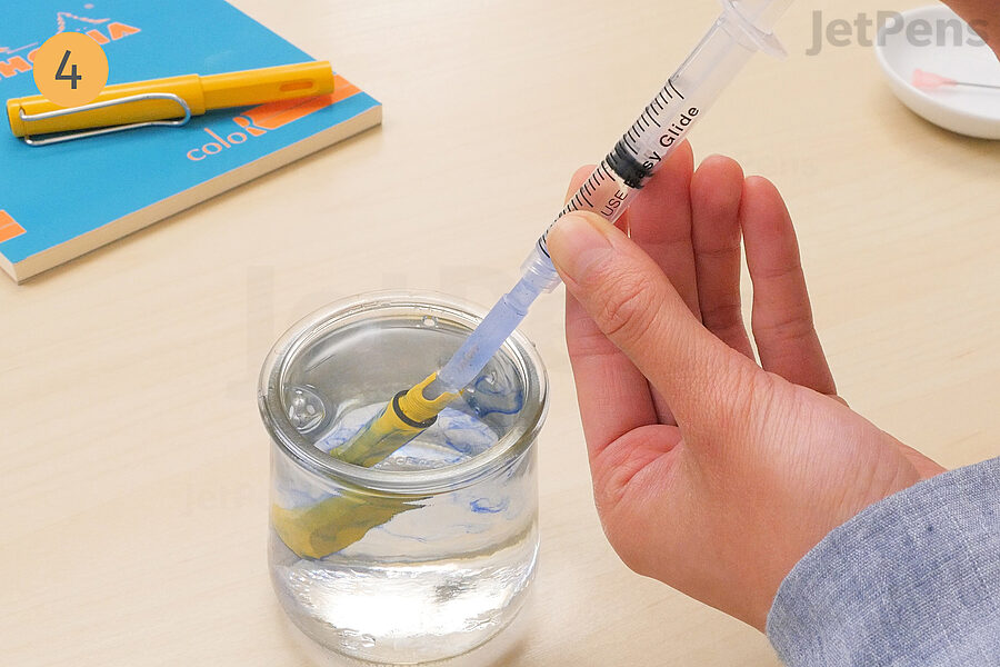 4. Dip the nib section into the cup and use the syringe to draw up water and flush the pen to clean.