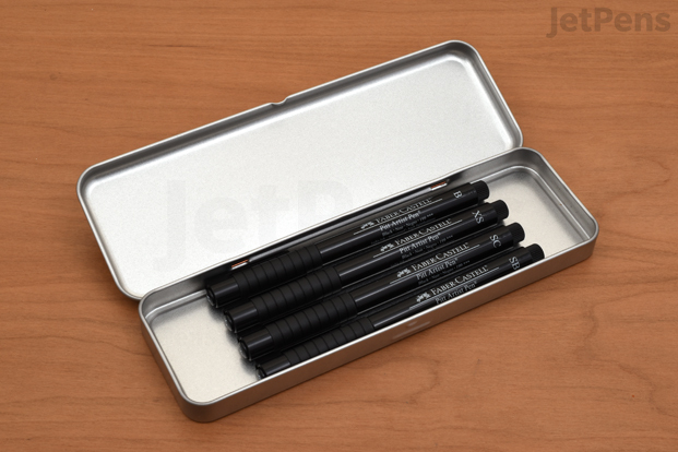 A selection of Faber-Castell PITT Artist Pens lying flat in a Velos Tin Pen Case.