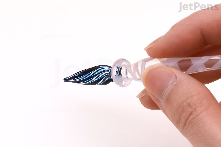 The spiraling tip of a glass dip pen, wet with orange ink.