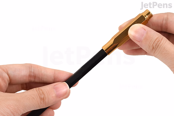 A person holding a Blackwing Point Guard Pencil Cap, Vol. 20 Limited Edition, which is a small, black cylindrical pencil accessory with a wooden, hexagonal-shaped top designed to protect the pencil tip.