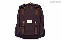 A grape-colored Doughnut Macaroon Standard Backpack with brown leather straps and gold-tone hardware, featuring a front zip pocket and a small white label on the lower front.