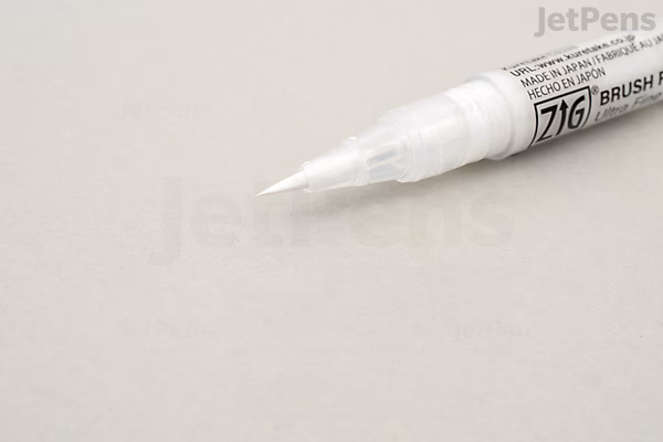 Close-up of a Kuretake ZIG Cartoonist Brush Pen with white ink and an ultra-fine brush tip on a light surface.
