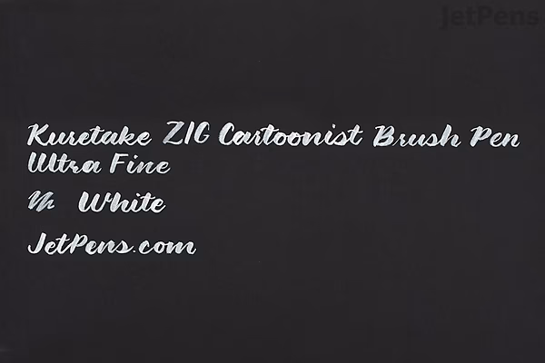 White ink writing on a black background that reads: "Kuretake ZIG Cartoonist Brush Pen Ultra Fine In White JetPens.com" in a cursive style.