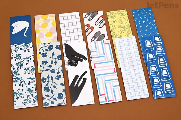 Six strips of King Jim Kitta Washi Tape with various patterns including birds, stationery, and airmail-themed designs, arranged side by side on a brown surface.