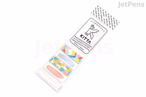 Three rolls of King Jim Kitta Washi Tape in a clear plastic package labeled "KITTA Washi Tape." The tapes feature colorful geometric patterns: one with pastel diagonal stripes, one with multicolored triangles, and one with pastel rectangles.