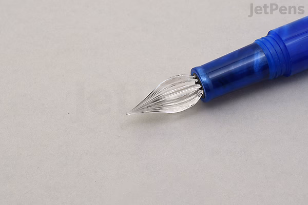 Close-up of a Majohn N6 fountain pen with an extra fine fude glass dip nib, featuring a marigold swirl design. The pen body is blue and the nib is clear glass with a curved, pointed shape.