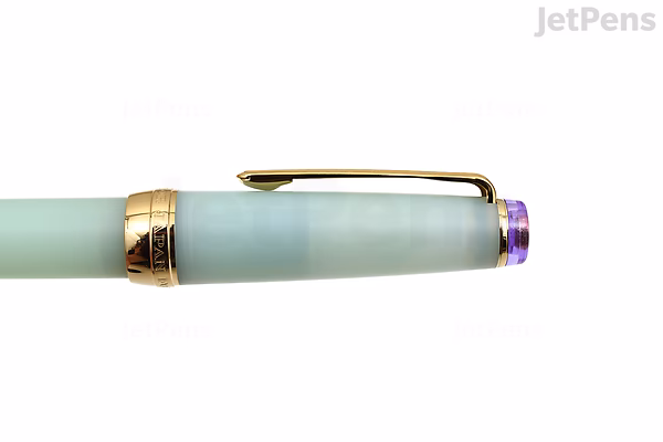 Close-up of a Sailor Pro Gear Slim Shikiori fountain pen in a soft pastel green color with gold accents, featuring a purple jewel on the cap top.