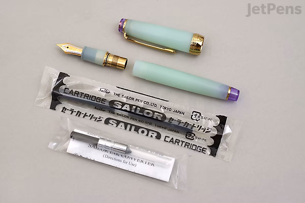Sailor Pro Gear Slim Shikiori Haru-same (Spring Rain) fountain pen with pastel blue-green barrel, gold trim, and 21k medium fine nib, shown disassembled with ink cartridges and converter on a light surface.