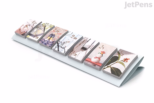 Himekuri Sticky Note Calendar 2022 displayed in a triangular stand, featuring daily tear-off sticky notes with various artistic illustrations and a matching booklet beside it.