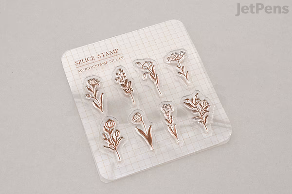 A clear plastic sheet containing eight small, delicate flower-shaped stamps arranged in two rows. The flowers have simple, elegant designs with thin stems and petals. The sheet is labeled "MU Clear Splice Stamp - My Icon - Flowers B (No. 15)."