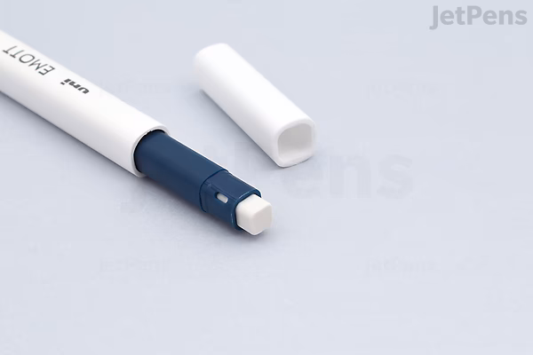 A close-up image of a Uni EMOTT Color Mechanical Pencil with a 0.9 mm lead size. The pencil is white with a dark blue grip section and has a white eraser exposed at the end, with its white cap removed and placed beside it on a light gray surface.