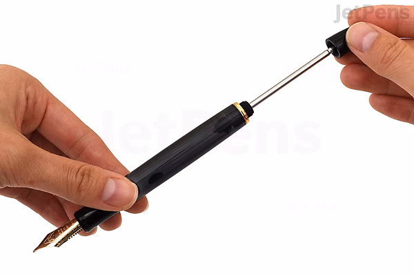 Photo showing a person inserting a converter into a Pilot Custom 823 fountain pen with an amber brown barrel and gold trim.