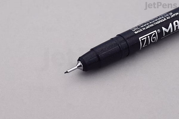 Close-up image of the fine tip of a black Zig marker pen on a light gray surface.