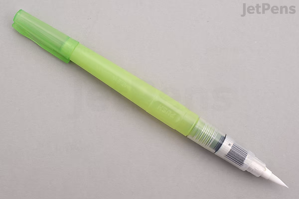 A green water brush pen with a translucent body and a white brush tip, lying horizontally on a light gray surface.