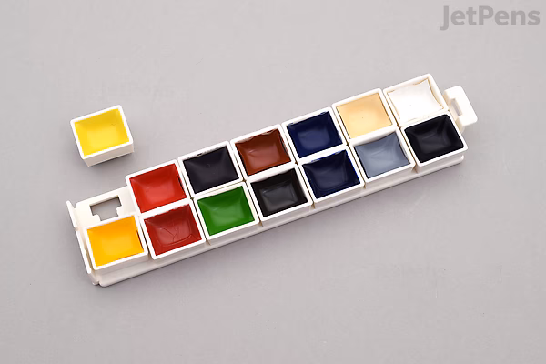 Kuretake Gansai Tambi Mini Watercolor Palette with 14 vibrant colors in a compact white plastic case, two pans removed and placed beside it.