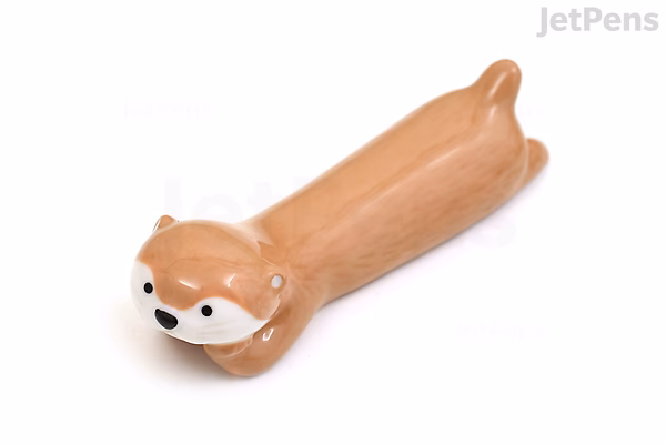 A beige ceramic pen rest shaped like a reclining otter with a rounded face and small ears.