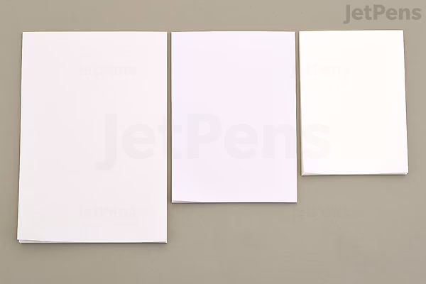 Three sheets of white paper of different sizes are arranged side by side on a gray surface, showcasing variations in texture and thickness.