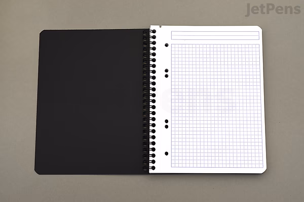 Spiral-bound Rhodia Greenbook notebook open to a graph paper page, showing a 6" x 8.3" size with a black cover on a gray surface.