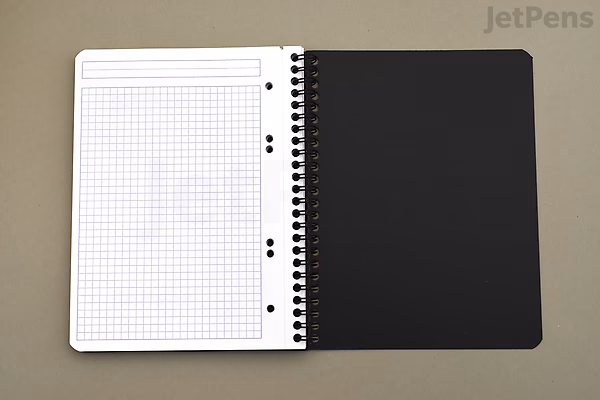 Open Rhodia Greenbook notebook showing a 6" x 8.3" graph paper page on the left and a black back cover on the right. The notebook has a spiral binding.
