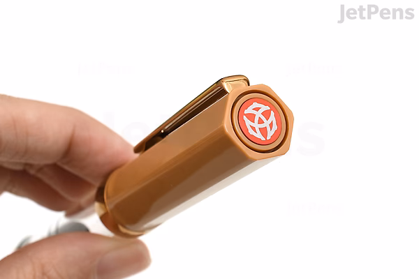 Close-up image of a hand holding the cap of a TWSBI ECO Caffè Bronze Limited Edition fountain pen with a 1.1 mm stub nib. The pen cap is bronze-colored with a glossy finish, featuring a clip and a red and white logo on the top.