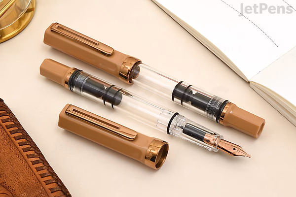 A TWSBI ECO Caffè Bronze Limited Edition fountain pen with a 1.1 mm stub nib, shown disassembled into four parts: cap, barrel, ink converter, and nib section. The pen features a transparent barrel and bronze-colored metal accents. It is placed on a light