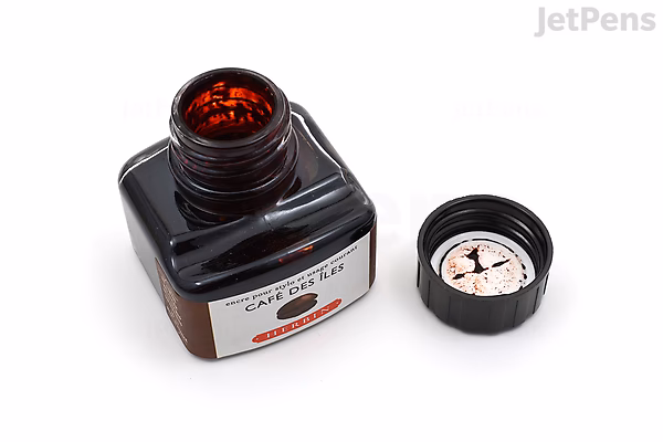 A 30 ml square glass bottle of Herbin Café des Îles ink (Island Coffee Brown) with the cap removed and placed beside it, showing the dark brown ink inside. The bottle has a white label with black and red text.