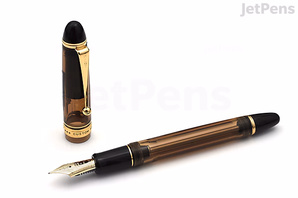 A Pilot Custom 823 fountain pen in amber brown with gold accents and a 14k fine nib, shown uncapped next to its cap standing upright.