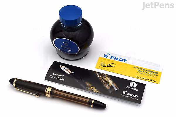 A Pilot Custom 823 amber brown fountain pen with gold accents, accompanied by a bottle of blue Pilot ink and two Pilot informational cards, all displayed on a white background.