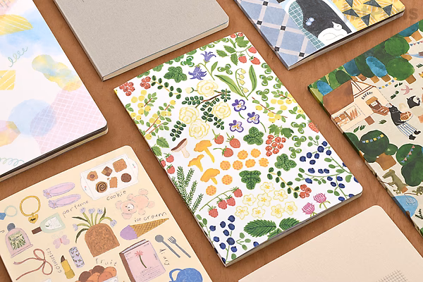 A B6-sized Midori Yuru Log Notebook with a cream MD paper featuring 5 mm dotted pages. The cover shows colorful illustrations of forest animals and plants, surrounded by other notebooks with various artistic covers.