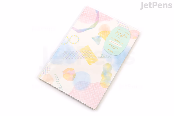 A B6-sized Midori Yuru Log Notebook with a cream-colored cover featuring a pastel watercolor design of geometric shapes and abstract patterns. The notebook has 5 mm dotted pages inside.